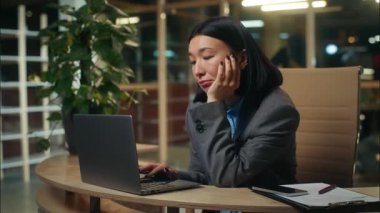 Sıkıcı Asyalı Çinli Japon kadın dizüstü bilgisayarla çalışıyor üzgün kız iş kadını işi ofis yöneticisinde aşırı çalışıyor sıkıcı işi nedensiz yere yoruyor.