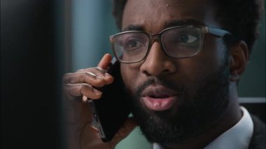 Yüzü kapatın, profesyonel Afro-Amerikan işadamı cep telefonundan konuşan, danışman, müşteri danışmanı, iş adamı ofisindeki monitör bilgisayarına bakan adam.
