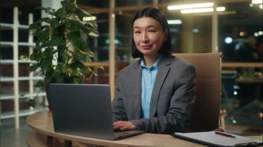 Mutlu Asyalı Koreli Çinli kadın dizüstü bilgisayar kullanarak çalışıyor kameraya bakıyor gülümseyen kadın portre ofis çalışanı iş kadını işveren ve online masa başı işvereni