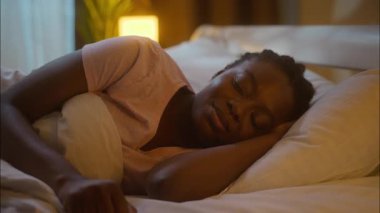 Huzursuz uyuyan Afro-Amerikalı sinirli bayan uykusuzluktan uykusuzluktan uyanıyor. Gece yarısı aydınlatılmış yatak odasındaki elektronik saat alarmı kontrol ediliyor.