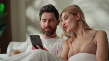 Pozitif Kafkasyalı çift, cep telefonu tutan erkek arkadaş kız arkadaş konuşan kız arkadaş yatak odasında internet oyunu yazan kız arkadaş yatak bağlantısı ortakları sabah kahvaltısı sipariş ediyor.