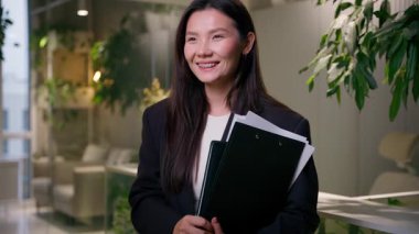 Gülümseyen etnik güzel kız Asyalı Koreli kadın iş kadını Çinli Japon iş kadını klasör belgelerini tutuyor mutlu kadın mimar simsar ofis içinde satıcı başı