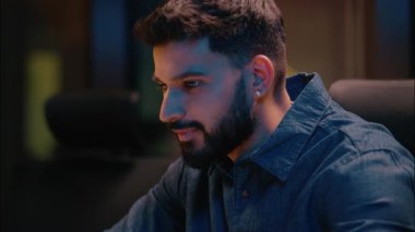 Gece bilgisayarı çalışmasında gülümseyen Hintli Arap işadamı erkek iş adamı ceo programcı yönetici girişimci karanlık akşam ofisinde dizüstü bilgisayar ticareti projesinde online daktilo