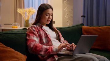 İş kadını genç kız öğrenciyi kullanarak ev yapımı iş bilgisayarı gece bağımlılığı bilgisayarını kullanarak beyaz bir kadınla evdeki kanepede online alışveriş sitesinde sohbet ederek.