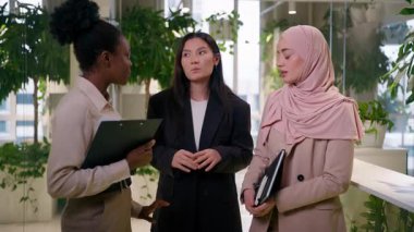 Çok ırklı iş kadınları, ofiste konuşan Afrikalı Asyalı kızlar üç farklı meslektaşla sohbet ederek Müslüman iş kadınlarının karın ağrısı çekmesine yardımcı oluyor.