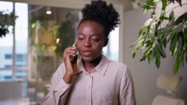 Gülümseyen iş kadını, Afrikalı Amerikalı etnik kız iş kadını ofiste cep telefonundan konuşan bayan işveren müdürü, akıllı telefondan arıyor cep telefonu sohbetleri yapıyor.