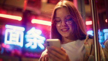 Neşeli, mutlu Asyalı Asyalı ergen cep telefonlu çocuk ekrandaki cep telefonuna dokunuyor neon öğrenci kız çocuk sanal oyun kızı oynuyor internette sosyal medya web kızı ile sohbet ediyor.