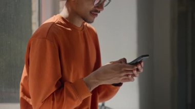 Afrikalı Amerikalı erkek öğrenci erkek öğrenci cep telefonuyla sohbet ediyor akıllı telefon ekliyor oyun sanal uygulaması sosyal medya oynuyor üniversite koridorunda modern teknolojiyi kaydırıyor.