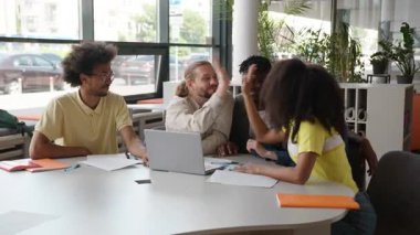 Bir grup çok ırklı öğrenci birlikte el ele vererek beşli jest işbirliği başarısını kutluyorlar liseli erkekler, liseli kızlar, üniversiteli erkekler, dizüstü bilgisayarla sınava hazırlanıyorlar.