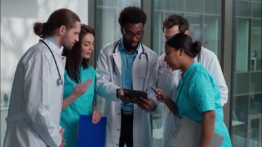 Çok kültürlü beş farklı insan Kafkas Hintli Afrikalı kadın erkek hemşireler dijital tablet cihazı arayan hemşireler birlikte danışmanlık yapan sağlık danışmanlığı yapan hastane koridorunda ayakta duran teşhis tavsiyelerine yardım ediyorlar.