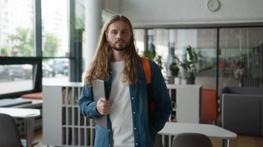 Ciddi, beyaz, düşünceli, Avrupalı, üniversite akademisinde poz veren, düşünceli, düşünceli, sakin, dizüstü bilgisayarlı, yalnız başına eğitim gören, öğrenim molası veren bir öğrenci.