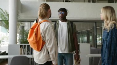 Üç üzgün, çok ırklı, ciddi, çok ırklı öğrenci arkadaşı üniversite koridorunda buluşuyor. Kafkasyalı kadın kız Afrikalı Amerikalı erkeklerle konuşuyor.