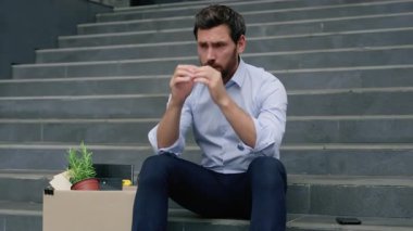 Orta yaşlı, olgun iş adamı erkek işveren üzgün bir şekilde ofis merdivenlerinde eşyalarıyla oturuyor ofis çalışanlarının attığı kutular şirkette işsizlik ekonomik krizine yol açıyor.