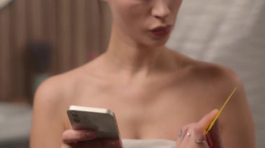 Havluya sarılı Kafkasyalı kadın havluyla banyodaki banka kartını tutuyor. İnternetteki ödeme hatası. Cep telefonu alım-satımı stresi yüzünden.