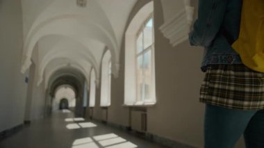 Sarı sırt çantalı öğrenci kızın boş koridor arkası. Üniversite öğrencisi kız öğrenci derslerine yalnız gidiyor. Üniversite koridorunda sabah tek başına yürüyor.