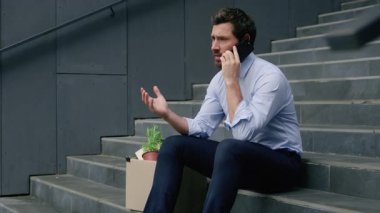 Orta yaşlı, işten çıkarma kutusuyla konuşan, cep telefonu tartışan, merdivenlerde oturan, iflas etmiş yetişkin işadamı işsiz kalmış, şehirdeki ekonomik krizden kovulmuş bir adam.