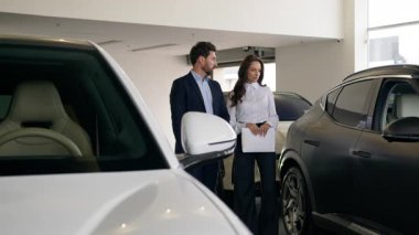 İki araba arasında seçim yapan beyaz bir adam kadın tüccar danışmanıyla iletişim kuruyor. Araba kiralama konusunda danışmanlık yapıyor. Otomobil salonu galerisinde araba kiralama servisini seçiyor.