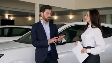 Kafkas erkek alıcı müşterisi otomobil kuaförü galerisinde kadın tüccar ile konuşuyor. Yeni lüks otomobil otomobili satın alan erkek araç taşıma test sürüşü test sürüşü kadın danışmanı seçimini tartışıyor.