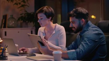 Kafkasyalı kadın Hintli erkek çok ırklı iş arkadaşları iş kadını iş arkadaşları iş arkadaşları dizüstü bilgisayar dijital tableti tasarımcıları gece ofisindeki çeşitli erkek sitesindeki cihazları kullanarak