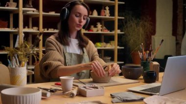 Kafkasyalı kadın ressam çanak çömlek atölyesi kadın ressam kadın ressam sanat tasarımcısı küçük kulaklık sahibi müzik çanak çömlekçi el yapımı kil çanak çömlek çiziyor.