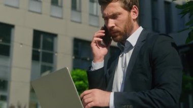 Ciddi iş adamı, olgun, orta yaşlı, çoklu görev sahibi, girişimci, akıllı telefon konuşmalarıyla şehir bilgisayarındaki iş belgelerini tutuyor.