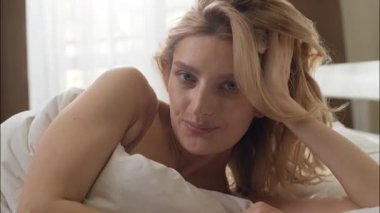 Gülümseyen beyaz kadın yatak odasında uzanıyor. Günaydın çekici bayan. Sabah uykusundan uyanan sağlıklı kadın.