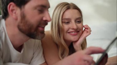 Gülümseyen beyaz aile çifti yatak odasındaki tablet uygulamaları kullanıyor. Konuşan erkek ekran teknolojisi aleti sabah partnerleri karı koca internette sanal oyun oynuyorlar.