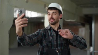 Gülümseyen Kafkasyalı mühendis mühendis cep telefonundan konuşan mimar bina inşaatı ustabaşısı işçi erkek işçinin akıllı telefon ile online sohbet ettiğini gösteriyor.