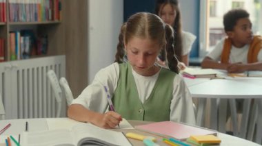 Gülümseyen mutlu, beyaz kız, kız, kız, okul çocuğu, okul öğrencisi, sınıf masasında ödev ödevi, ilköğretim dersi, çocuklar kameraya bakarak pozitif öğrenme eğitimi alıyorlar.