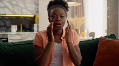 Heyecanlı, Afro-Amerikalı, etnik kadın, mutlu, model, ev sahibi, inanılmaz haberler duyan, ağzı açık, kanepe kanepesinde oturma odasında oturan hayret verici, hayret verici, hayret verici bir şey.