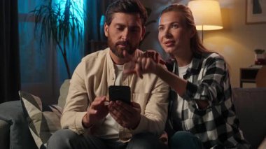 Kafkas aile çifti, kanepenin üzerinde akıllı telefon cihazı kullanıyor. Kız arkadaş, erkek arkadaş, internet alışverişi, karı-koca, cep telefonu uygulamasını seçiyor.