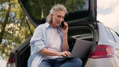 Kafası karışmış Kafası karışmış Kafkasyalı büyükanne iş kadını olgun bir iş kadını dizüstü bilgisayar sorunu kullanıyor cep telefonu aranıyor park yerinde arabasının bagajında oturan polis memuruyla konuş.