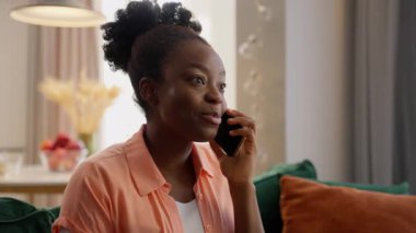 Mutlu Afrika kökenli Amerikalı kadın model ev sahibi müşterinin cep telefonu konuşması gülüşü dostça konuşma konuşması evde kapalı salonda akıllı telefon konuşması.