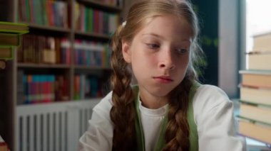 Öfkeli, sinirli, umutsuz, Kafkas, küçük, kız, öğrenci, iki yığın kitap arasında sınıf masasında oturuyor. Ev ödevi yapmak zor.