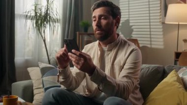 Üzgün adam kanepenin sahibi cep telefonunu karıştırıyor kötü haber mesajı akıllı telefon evde endişeli cep telefonu dolandırıcılığı yapan endişeli erkek işadamı hayal kırıklığına uğrattı.