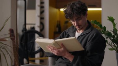Odaklanmış Kafkasyalı adam evde kitap okuyor. Hippi erkek, kitap okuyor. Edebiyat, bilgi kütüphanesi hobisi öğreniyor.