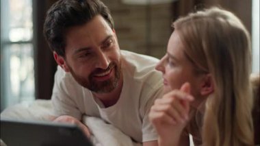 Aile gülen beyaz bir çift yatak odasında tablet kullanıyor. Koca internetten ortaklar tutuyor. Sabah karı koca internetten alışveriş yapıyor.