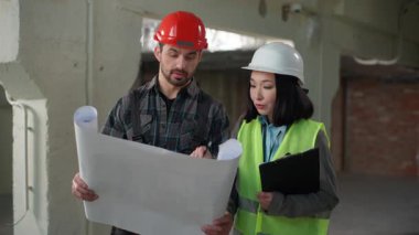 Çok ırklı iki inşaatçı Japon kadın Kafkasyalı planlı inşaat mühendislerini tartışıyor kağıt başıyla kafa sallıyor, mimarlarla konuşuyor takım çalışması projesi inşaatı yapıyor.