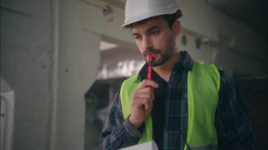 Düşünceli Kafkasyalı mimar erkek elektrikçi müteahhiti, mühendisin elinde not defteri tutan teknisyenin mimari proje taslağı hazırladığını düşünüyor.