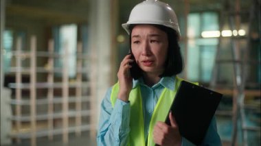 Asyalı kadın inşaatçı mimar Çinli mühendis usta teknisyen elektrikçi kız Koreli bayan Japon kadın müfettiş kasketli endüstriyel işçi kapalı alanda cep telefonu inşaatında çalışmaktan hoşnutsuz.