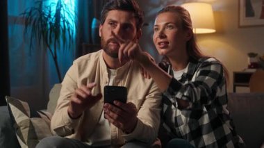 Beyaz bir aile çifti, akşam evde akıllı telefon kullanıyor. Kanepede internetten alışveriş yapıyor. Koca, karı, kız, internet satın alıyor.