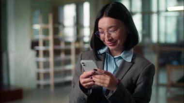 Mutlu gülümseyen Asyalı kadın Çinli işkadını mimar iş adamı cep telefonundan mesaj atan sosyal medya bağımlısı Koreli Japon bayan kullanıcı akıllı telefonu ofiste çalışıyor.