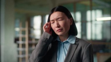 Asyalı iş kadını baş ağrısı çekiyor. Yorgun Çinli kız Koreli kadın çalışan yönetici ofiste çok çalışıyor. Baş şakaklarına masaj yapıyor.