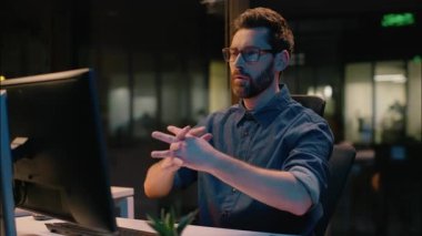 Kafkasyalı iş adamı çevrimiçi olarak işini bitirdi, fazla mesai yaptı, bilgisayar işini bitirdi, çok çalıştı, gece ofisinde yorgun bir erkek, ellerini dinlendirip kafa dinlendirdi.