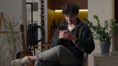 Mutlu İspanyol adam cep telefonu ekranını ev istemcisinde yazıyor. Cihaz teknolojisi kullanan, gülen adam kullanıyor. Hipster eşya satın alıyor.