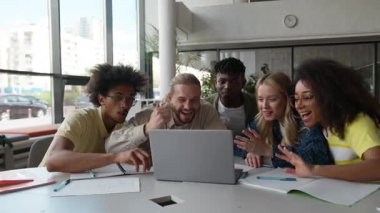 Çok kültürlü öğrencilerden oluşan bir grup mutlu bir sevinç iyi sonuç geçişini kutluyor takım çalışması başarısı liseli erkekler kız çocuklar üniversitede dizüstü bilgisayarla gülüyor