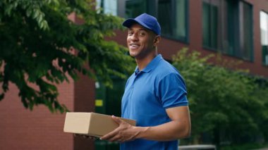 Mutlu Afro-Amerikan gülen adam teslimatçı erkek kurye paketçi dükkan paketi teslimat şehir mesleğinde kargo alışverişi kamera siparişine bakan müşteri ver