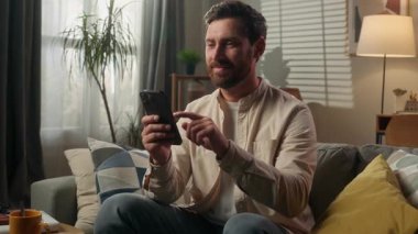 Kafkasyalı adam, modern uygulama erkek, gülümseyen iş adamı, ev sahibi rahat, akıllı telefon cihazını kullanıyor. Çevrimiçi alışveriş merkezi siparişi veriliyor.