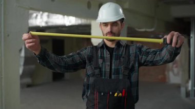 İnşaatçı mimar elinde ölçü cetveli tutuyor. Metre ölçer ölçer, beyaz erkek müfettiş ustabaşı tamirci, tamirat mühendisi inşaat teftişi için ölçü aleti boyutu kullanıyor.