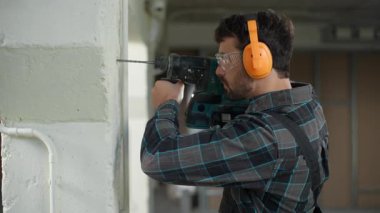 İnşaat mühendisi, matkap onarım binası inşaatı, beyaz erkek ev mimarı, elektrikçi, elinde elektrikli aletle delme deliği tutan bir inşaat mühendisi.